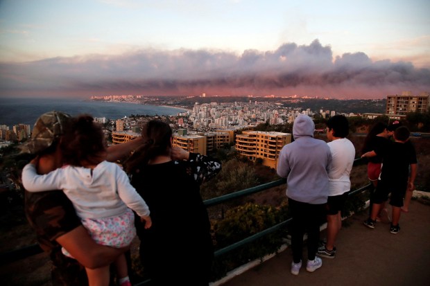TOPSHOT - Residents of a Valparaiso neighborhood look at the cloud of smoke produced by forest fires in Viña del Mar on February 2, 2024. A huge mushroom cloud of smoke hangs over tourist areas in central Chile, including Viña del Mar and Valparaiso, where a forest fire broke out on Friday, threatening hundreds of homes and forcing the evacuation of residents. (Photo by Javier TORRES / AFP) (Photo by JAVIER TORRES/AFP via Getty Images)