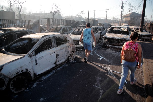 People walk next to burnt vehicles after a fire that affected the hills in Viña del Mar, Chile on February 3, 2024. The region of Valparaoso and Viña del Mar, in central Chile, woke up on Saturday with a partial curfew to allow the movement of evacuees and the transfer of emergency equipment in the midst of a series of unprecedented fires, authorities reported. (Photo by Javier TORRES / AFP) (Photo by JAVIER TORRES/AFP via Getty Images)