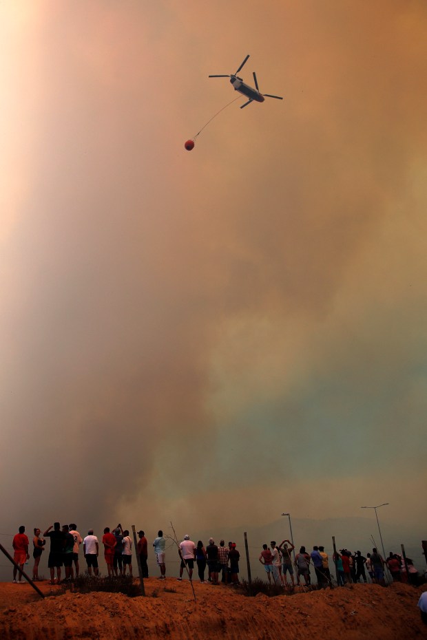 A helicopter puts out a forest fire affecting the hills in Quilpe comune, Valparaiso region, Chile on February 3, 2024. The region of Valparaoso and Viña del Mar, in central Chile, woke up on Saturday with a partial curfew to allow the movement of evacuees and the transfer of emergency equipment in the midst of a series of unprecedented fires, authorities reported. (Photo by Javier TORRES / AFP) (Photo by JAVIER TORRES/AFP via Getty Images)