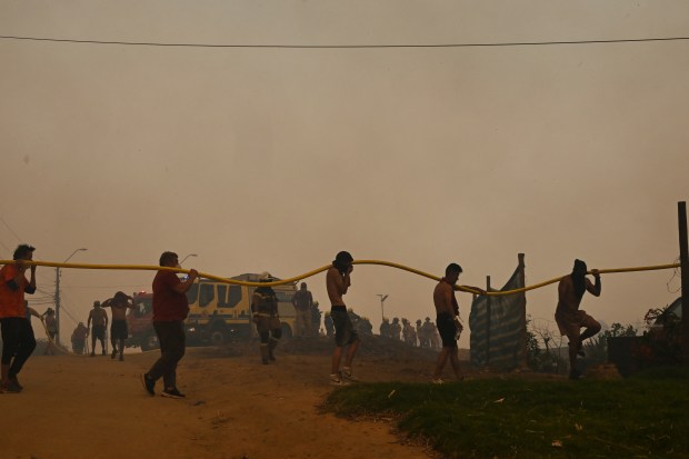 Residents help firefighters during a forest fire affecting the hills in Quilpe, Valparaiso region, Chile, on February 3, 2024. The region of Valparaoso and Viña del Mar, in central Chile, woke up on Saturday with a partial curfew to allow the movement of evacuees and the transfer of emergency equipment in the midst of a series of unprecedented fires, authorities reported. (Photo by RODRIGO ARANGUA / AFP) (Photo by RODRIGO ARANGUA/AFP via Getty Images)
