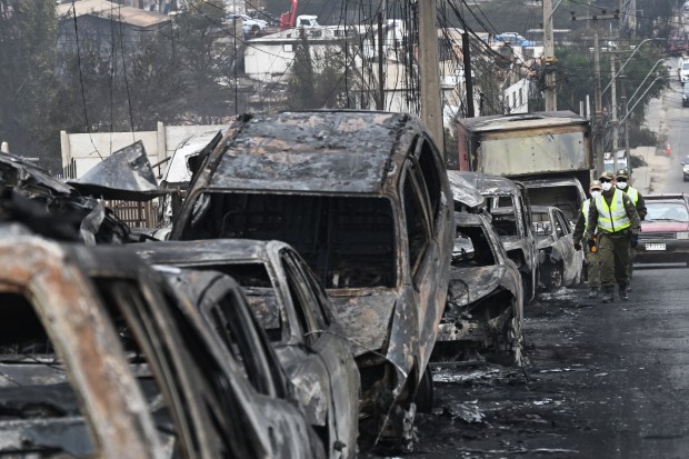 TOPSHOT - Chilean 'carabineros' walk past burned vehicles after a forest fire in Quilpue, Viña del Mar, Chile, on February 4, 2024. Chileans Sunday feared a rise in the death toll from wildfires blazing across the South American country that have already killed at least 51 people, leaving bodies in the street and homes gutted. (Photo by RODRIGO ARANGUA / AFP) (Photo by RODRIGO ARANGUA/AFP via Getty Images)
