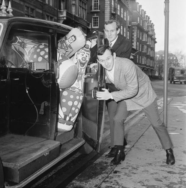 American musicians and comedians the Smothers Brothers, aka Dick (foreground) and Tom Smothers, struggle to fit inflatable toys into a taxi, 23rd December 1967. (J. Wilds/Keystone/Hulton Archive/Getty Images)