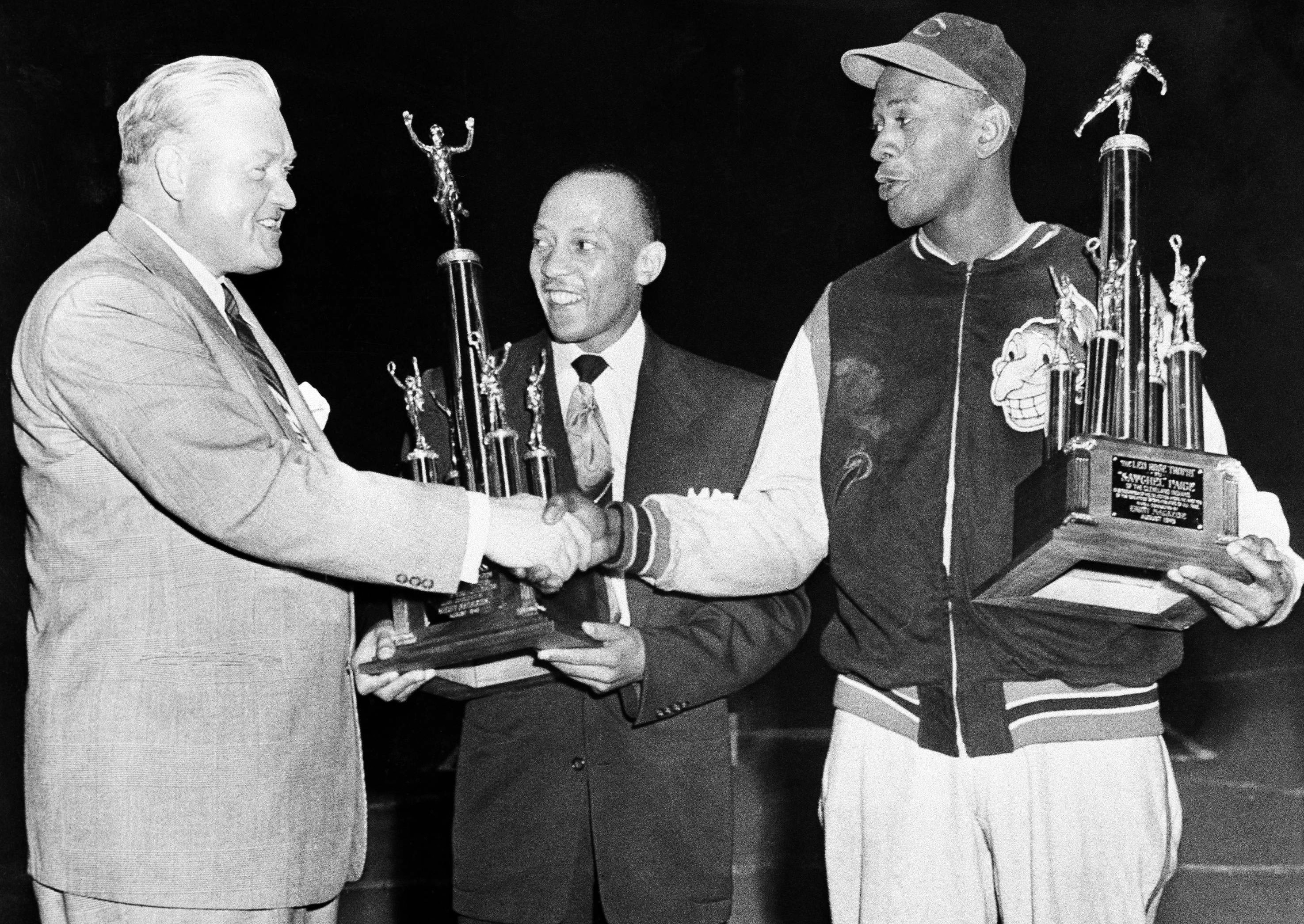 Jesse Owens (C) and pitcher Satchel Paige of the Cleveland Indians are congratulated by State's Attorney John Boyle, left, upon winning trophies for finishing first and fourth respectively in a nation-wide poll on outstanding Black athletes on Aug. 19, 1949. The presentation of the trophies were made at Comiskey Park in Chicago at a Cleveland-Chicago White Sox game.